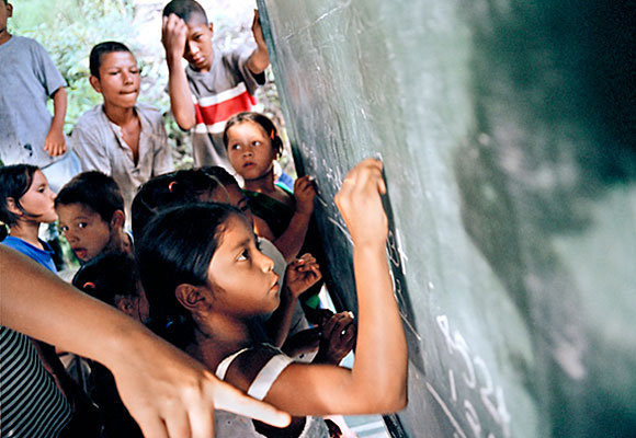 photograph of child writing on chalkboard in class