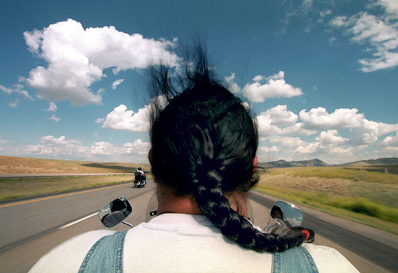 photograph: man riding a Harley Davidson motorcycle, helmetless, hair blowing upward